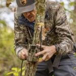 hunter setting up trail camera on tree