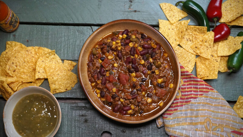 venison chil in a bowl with salsa chips around it