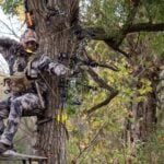 Bowhunter at full draw sitting in treestand