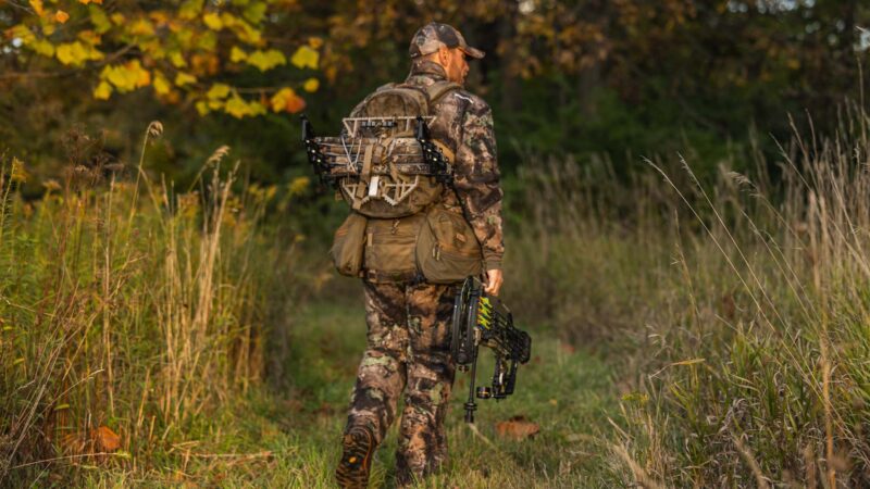 Bowhunter walking through a grass field on a mowed path.