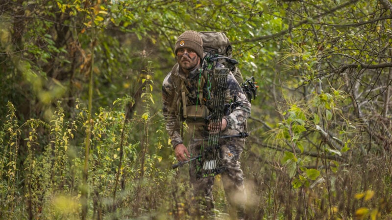 hunter walking in woods with bow