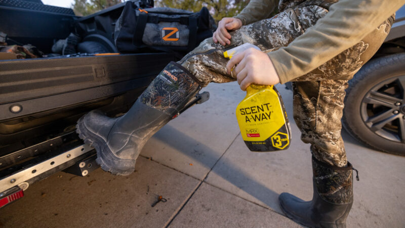 hunter spraying boots with scent killer spray bottle