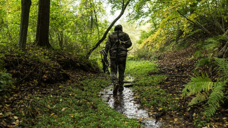 deer hunter walking down creek with bow in hand