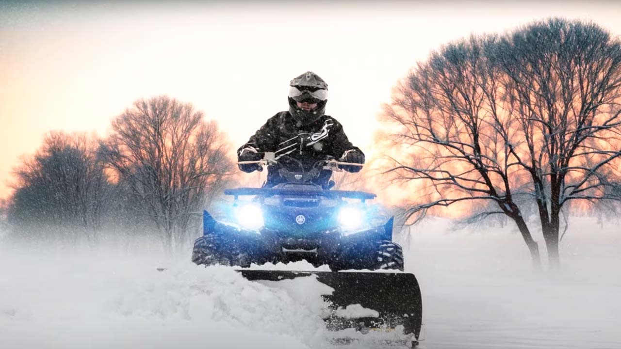 Man driving an ATV with a snowplow on the front.