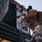 Bowhunter climbing up a ladder and entering a Muddy box blind.