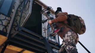 Bowhunter climbing up a ladder and entering a Muddy box blind.